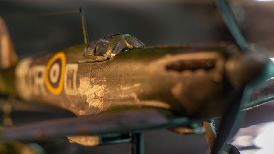 A close-up image of a vintage military aircraft model, primarily painted in a weathered green finish with visible signs of age and wear. The canopy is made of clear plastic, showing some scratches and